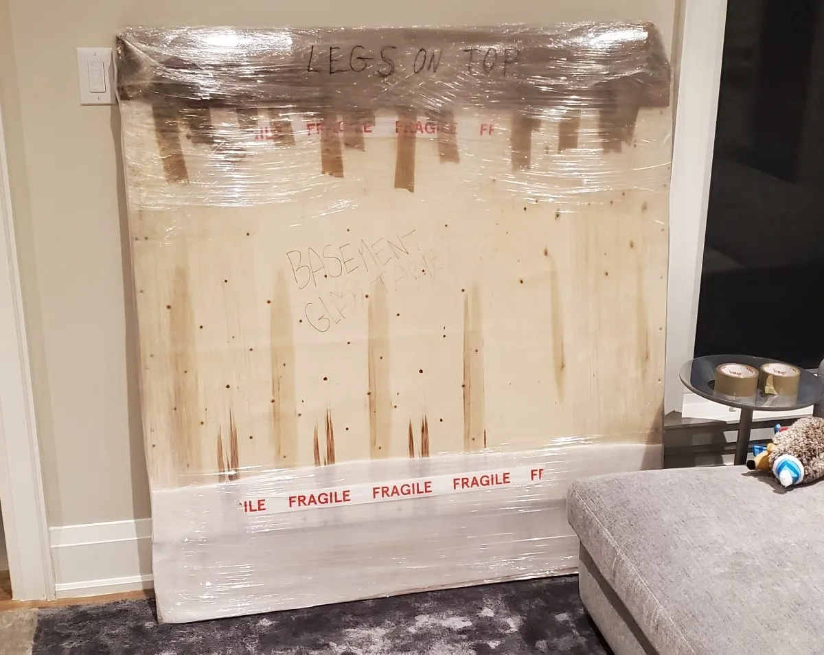 Wooden dresser wrapped in clear plastic and padding, marked with red FRAGILE tape for a move